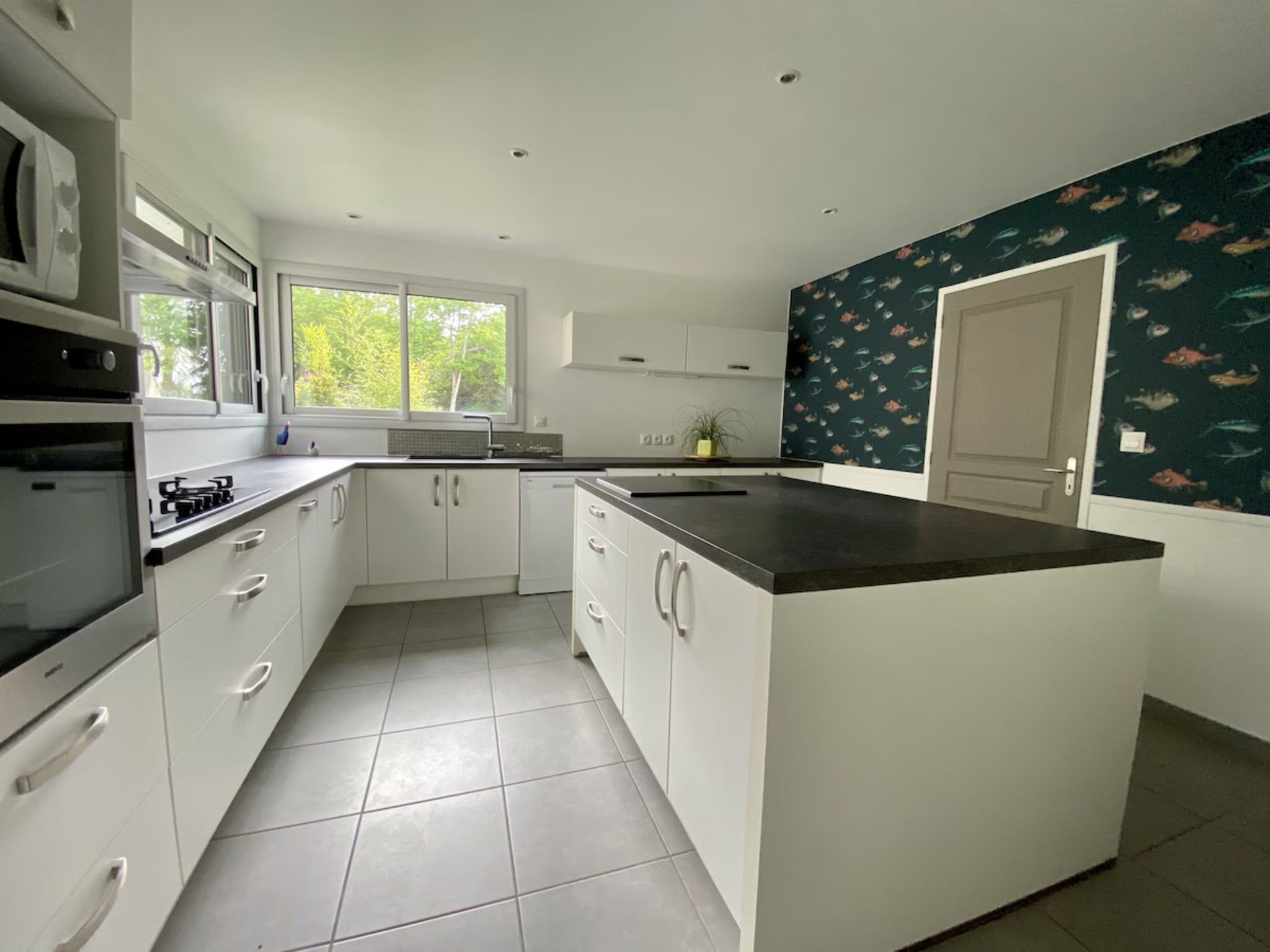 A modern kitchen with white cabinetry, a large island, and a window providing natural light.