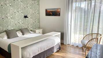 A bedroom with a bed, a nightstand, a chair, a painting, and a window with curtains.