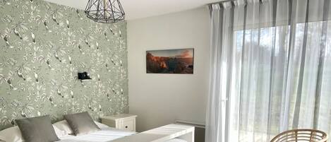 Ein Schlafzimmer mit einem Bett, einem Nachttisch, einem Sessel, einem Gemälde und einem Fenster mit Vorhängen.