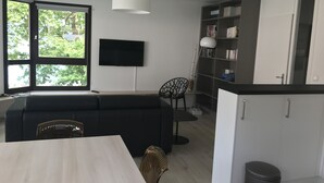 Ein modernes Wohnzimmer mit Sofa, Esstisch, Bücherregal und Fernseher.
