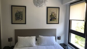 Ein Schlafzimmer mit einem großen Bett, zwei gerahmten Bildern an der Wand, einem Fenster mit Aussicht und einer Deckenleuchte.