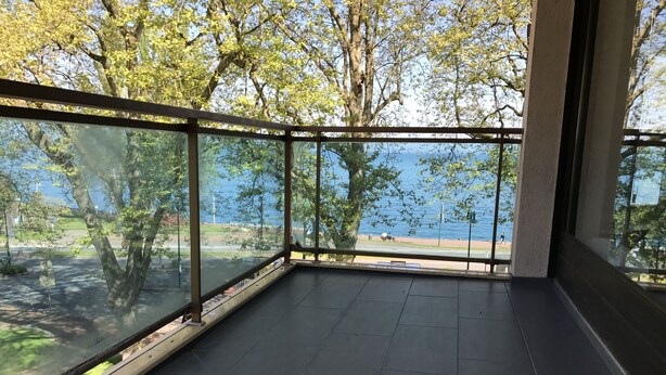 Ein Zimmer mit großen Glasfenstern und Blick auf ein Gewässer und Bäume.
