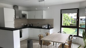 Eine moderne Küche mit weißen Schränken, einer schwarzen Arbeitsplatte und einem Essbereich mit Holztisch und Korbstühlen.