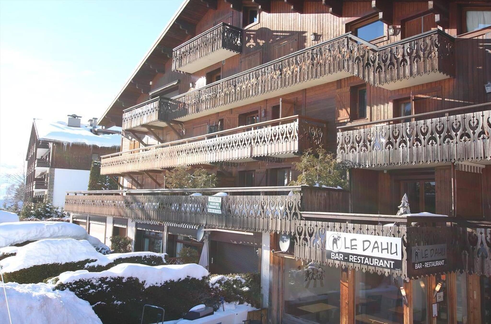 A multi-story building with balconies, a sign for 'LE DAHUI BAR - RESTAURANT', and snow-covered surroundings.