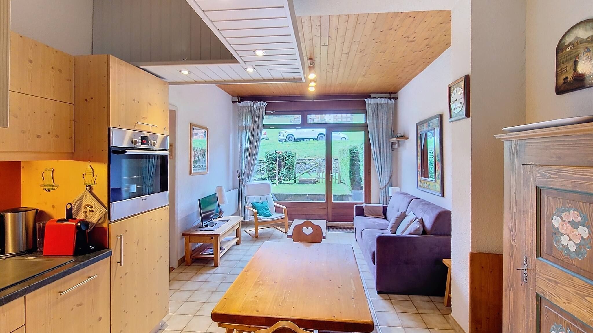 A compact kitchen with modern appliances, a dining area with a wooden table, and a seating area with a sofa and armchairs.