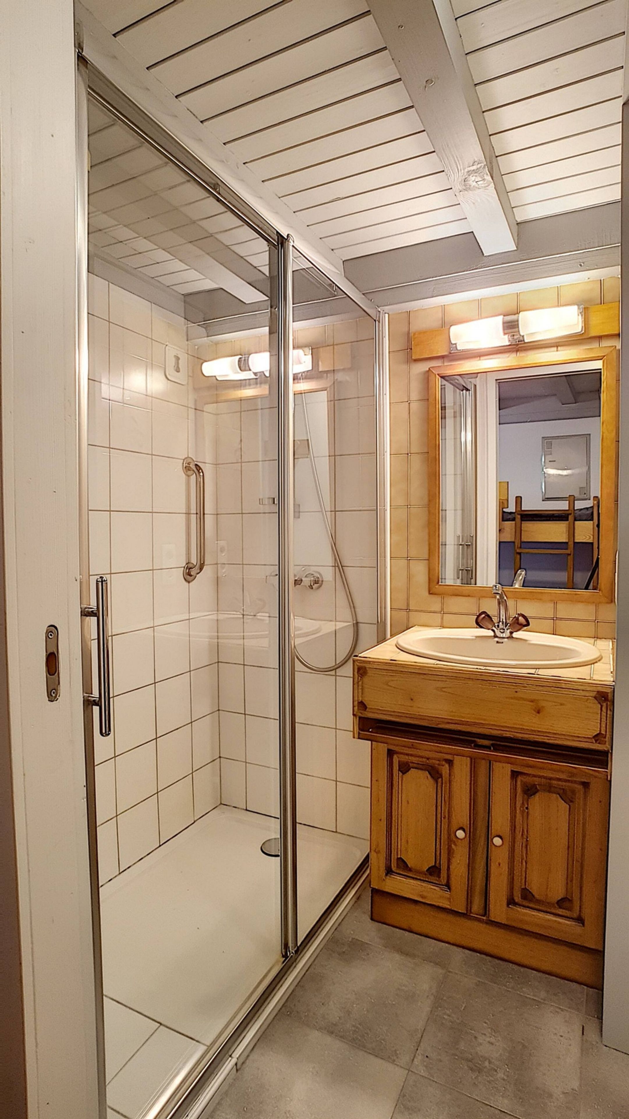 Un bagno con box doccia in vetro, un mobile bagno in legno con lavandino e uno specchio sopra il mobile.