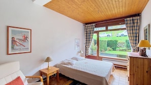 A bedroom with a bed, a nightstand, a lamp, a chair, and a window with curtains.