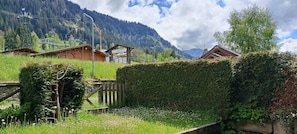 A mountain cabin with a wooden exterior, surrounded by lush greenery and a clear sky.