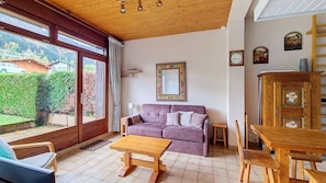 A living room with a sofa, a wooden table, and a view of a garden through large windows.