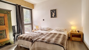 A bedroom with two beds, a window with curtains, a wall-mounted picture, and bedside lamps.