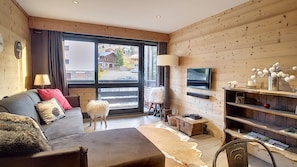 A cozy living room with a sofa, a small white stool, a television, and a fireplace.