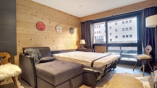 A modern hotel room with a bed, a seating area, and a window with a city view.