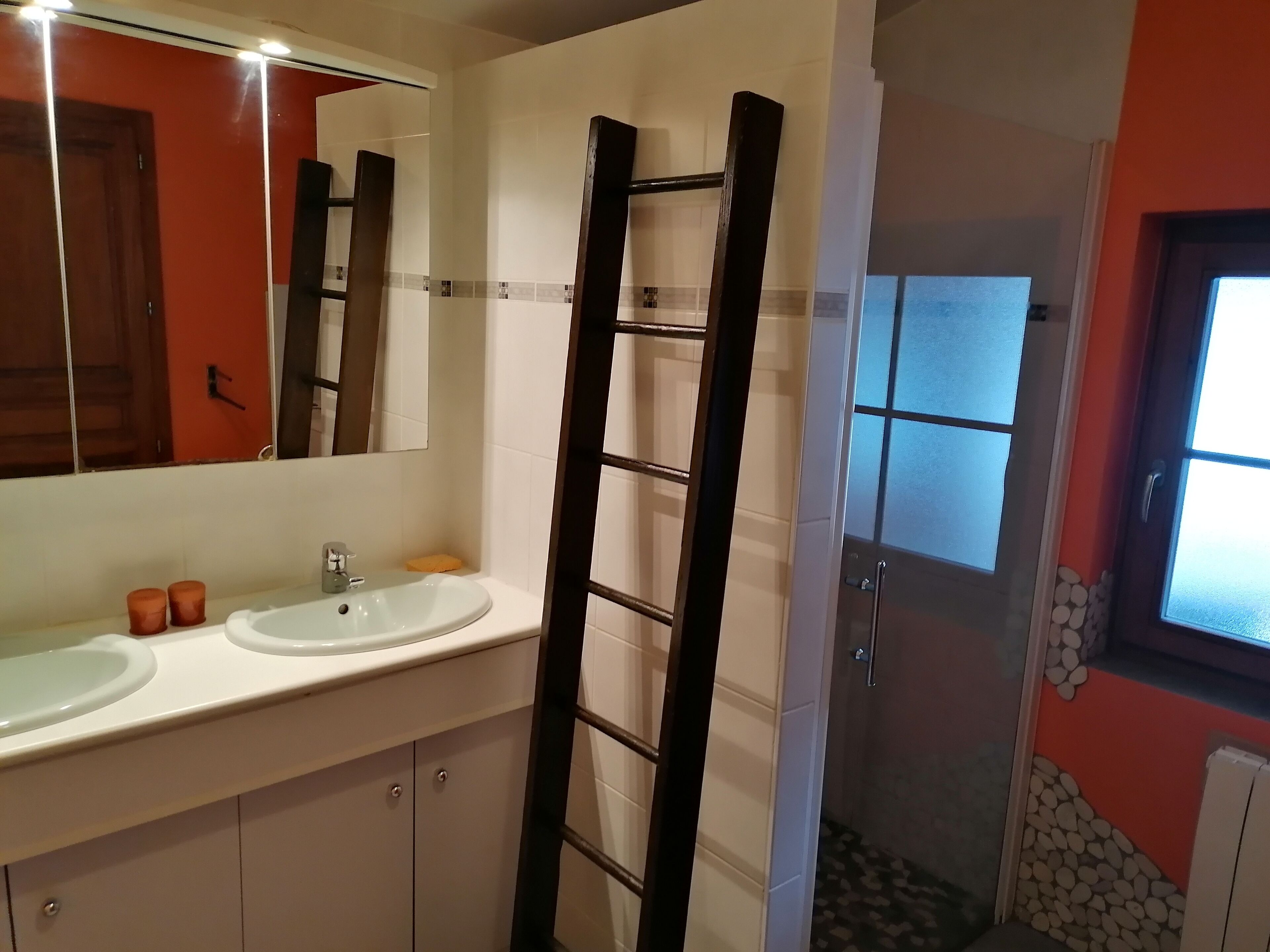 Un baño con lavamanos blanco, espejo y dos recipientes cilíndricos marrones.