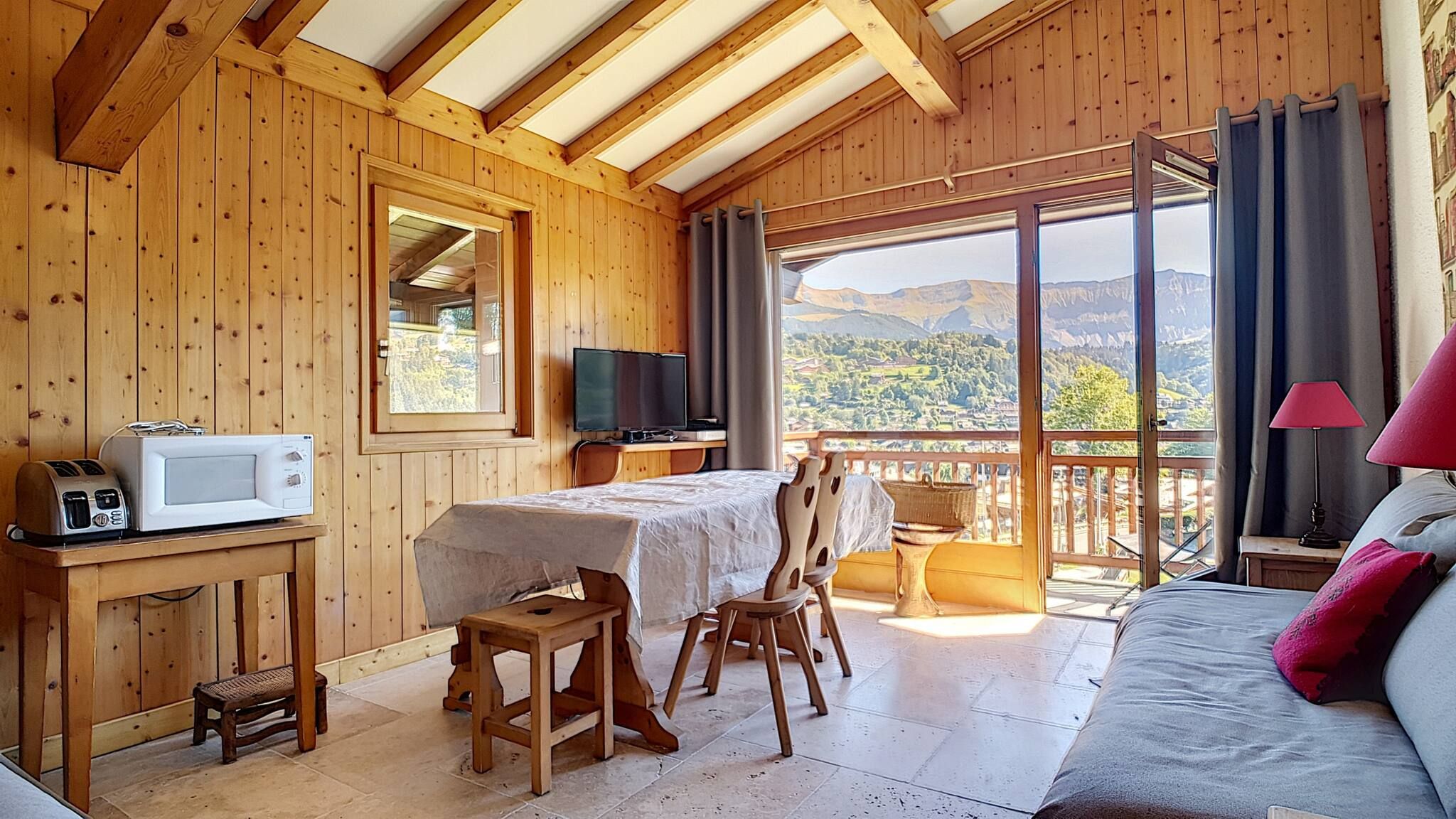 Una cabaña de madera con balcón, una mesa de comedor, un televisor y una cama.