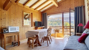 A wooden cabin with a balcony, a dining table, a TV, and a bed.