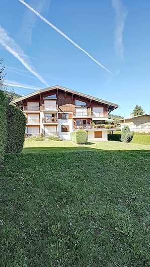 A multi-story building with balconies, a well-maintained lawn, and a clear sky. - Apartment rental near the slopes in the Jaillet area (Megève)