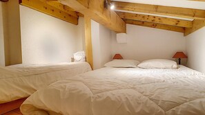 Un dormitorio con dos camas, vigas de madera, paredes blancas y dos lámparas de noche.