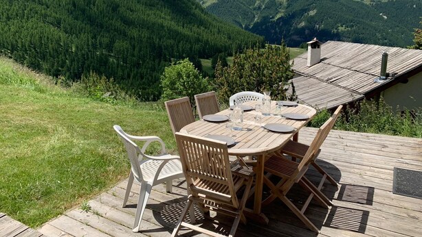 A wooden deck with a table and chairs overlooking a mountainous landscape.