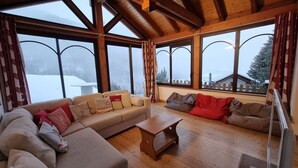 A cozy living room with a wooden ceiling, large windows, a sofa set, and a coffee table.
