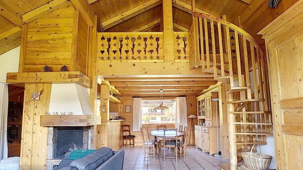 A wooden cabin interior with a fireplace, a dining area, and a staircase. - 1 Chalet Clarines (Megève)