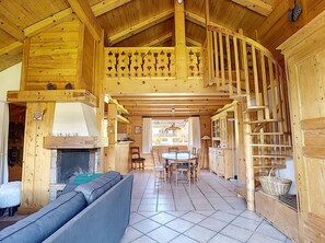 Interior de una cabaña de madera con chimenea, comedor y escalera.