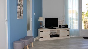 Een kamer met een televisie op een houten kast, een deur met een bordje en een raam met gordijnen.