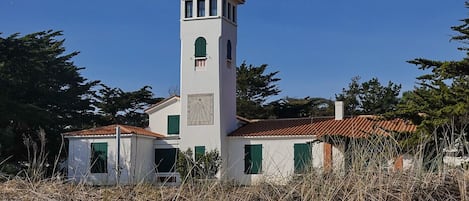 A white building with a tall tower, green shutters, and a tiled roof.