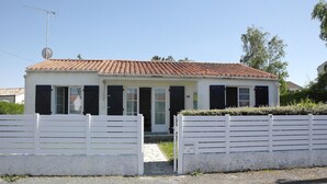 Een gelijkvloers huis met een pannendak, witte buitenmuren en zwarte luiken. Op het dak staat een schotelantenne en op de voortuin een brievenbus.