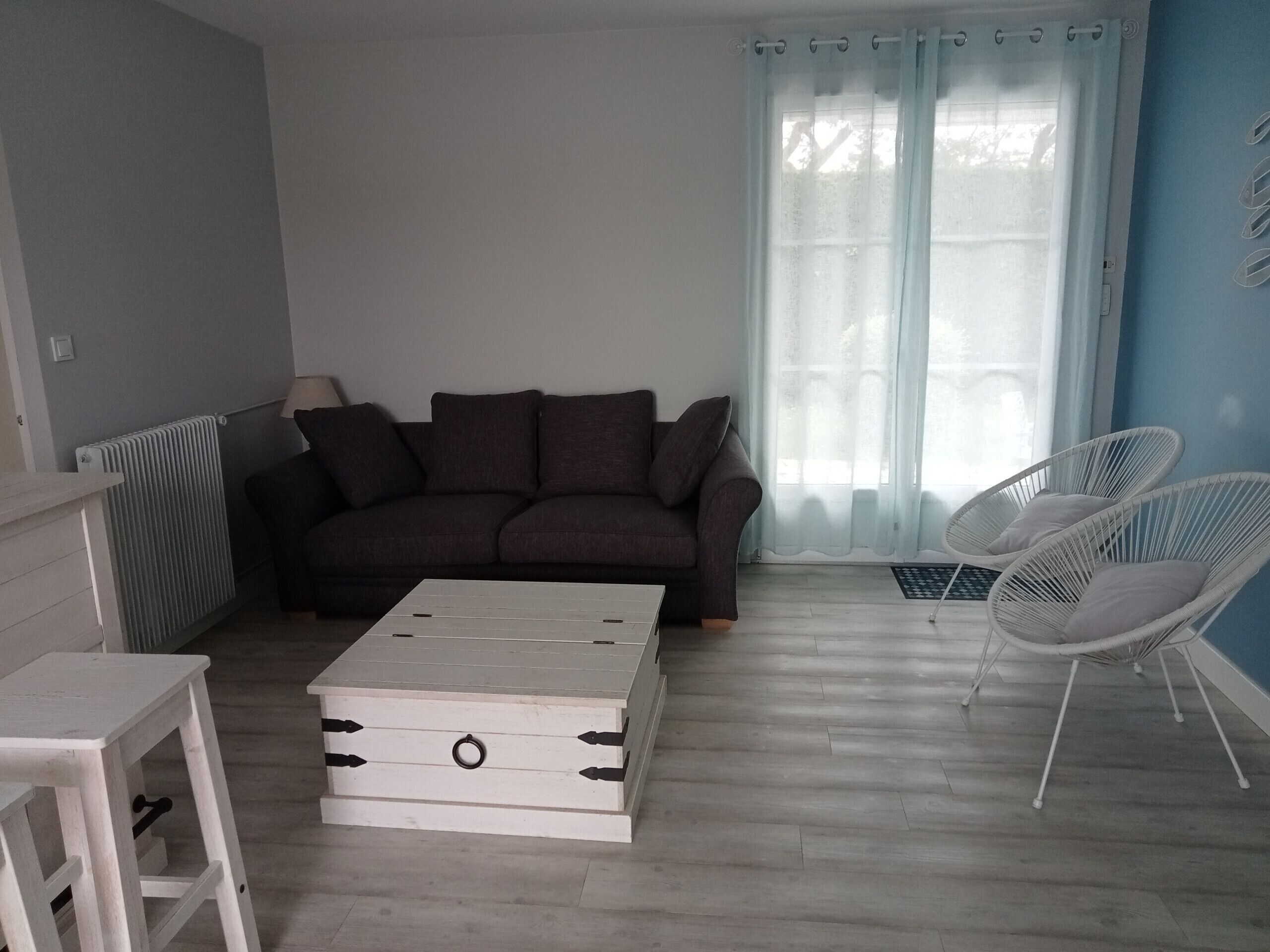 A living room with a dark grey sofa, a white chest of drawers, and two white wicker chairs.
