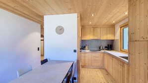 Une cuisine de taille réduite, avec des meubles de rangement en bois, une table à manger et une horloge au mur.