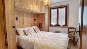 Une chambre à coucher aux murs lambrissés, avec un lit, une fenêtre avec des rideaux et une chaise.