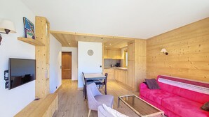 Un intérieur en bois comprenant un téléviseur, un canapé rouge, une table à manger et un coin cuisine.