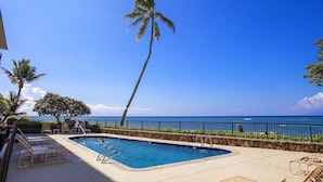 A swimming pool with lounge chairs, a palm tree, and a view of the ocean.