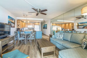 A modern living room with a sofa, TV, wooden coffee table, and a dining area with chairs and a table.