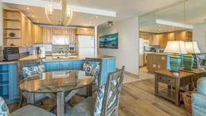A modern kitchen with wooden cabinets, a central island, and a dining area with a glass table and blue chairs.