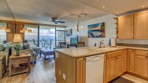A modern kitchen with wooden cabinets, a dishwasher, and a dining area with a view of the ocean.
