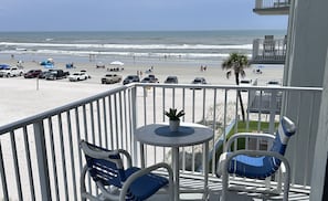A balcony with a table and chairs overlooking a beach with parked cars and people. - Oceanfront Corner Wraparound Balcony Condo Ocean Reef 311 - (New Smyrna Beach)