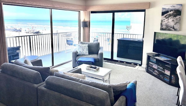A living room with a balcony overlooking a beach, a television, and a bookshelf.