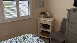Ein Schlafzimmer mit einem Bett, einem Sessel, einem Schminktisch und einem Fenster mit Jalousien.