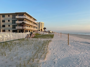 A beachfront hotel with multiple balconies, a sandy beach, and a clear sky.