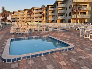 A swimming pool area with multiple pools, lounge chairs, and a building with balconies in the background. - Oceanfront Corner Wraparound Balcony Condo Ocean Reef 311 - (New Smyrna Beach)