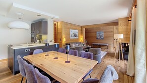 Une cuisine moderne dotée d’un îlot central, d’un coin repas avec une table et des chaises en bois, et d’un espace salon confortable avec un canapé et des fauteuils.