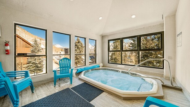 A spa area with a hot tub, two blue chairs, and large windows offering a view of snow-covered trees and mountains. - Newly Renovated, One Bedroom Condominium at Purgatory Steps From Slopes (Durango)