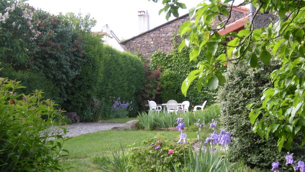 Un jardin bien entretenu, agrémenté de diverses plantes et fleurs, un mur en pierre et un espace aménagé avec des chaises et une table.