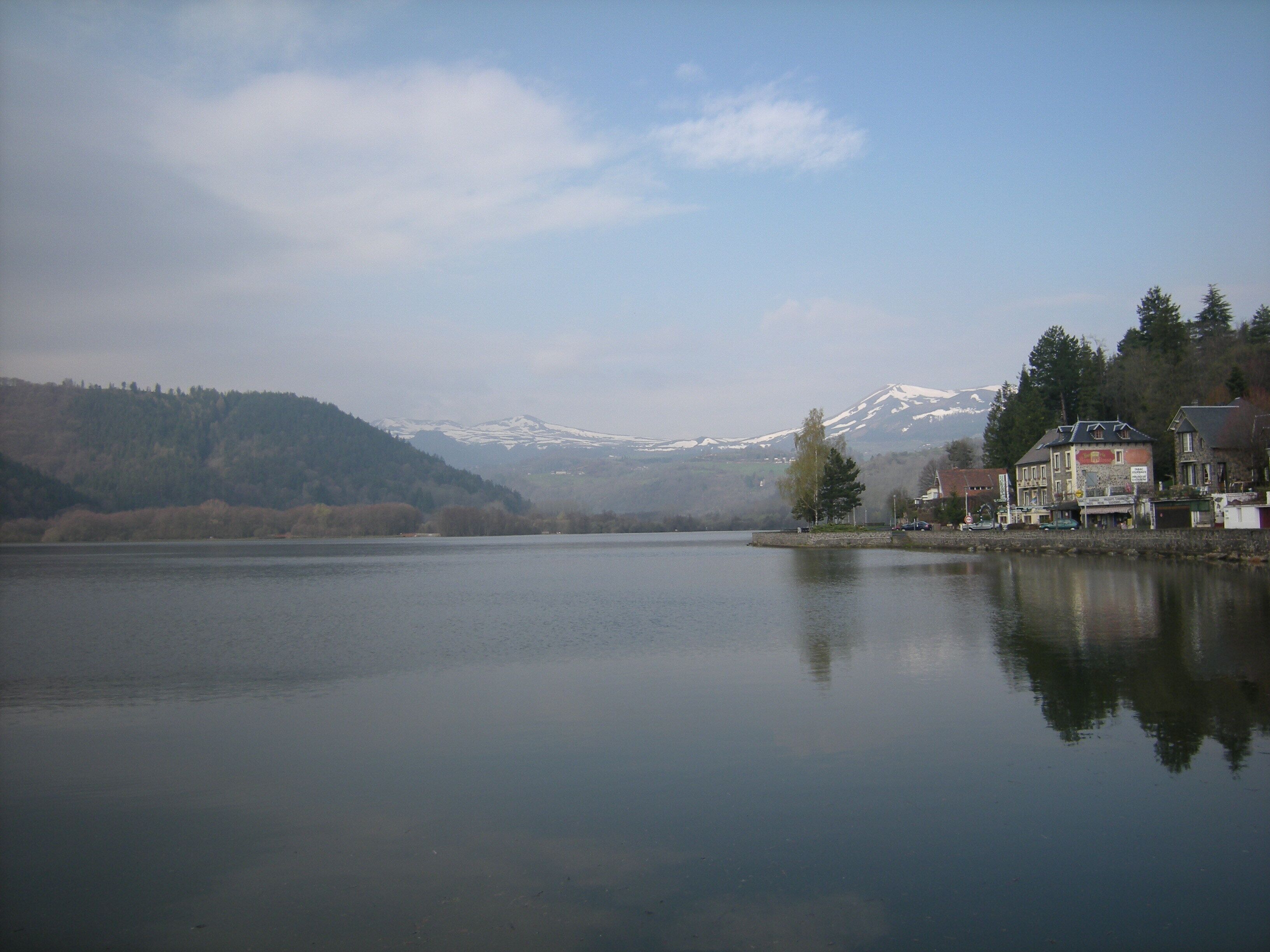 Un lac paisible, avec une montagne en arrière-plan et une rangée de bâtiments le long de la rive.