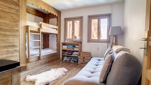 Una habitación acogedora con una cama litera, un sofá, una estantería y una ventana.