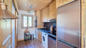 Cocina compacta con armarios de madera, un refrigerador de acero inoxidable, lavadora y una ventana que proporciona luz natural.