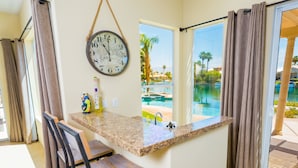A room with a kitchen counter, a dining area with chairs, a clock, and a view of a pool. - Executive Lakefront La Quinta Gem with Infinity Pool, Boats, and Casita (La Quinta)