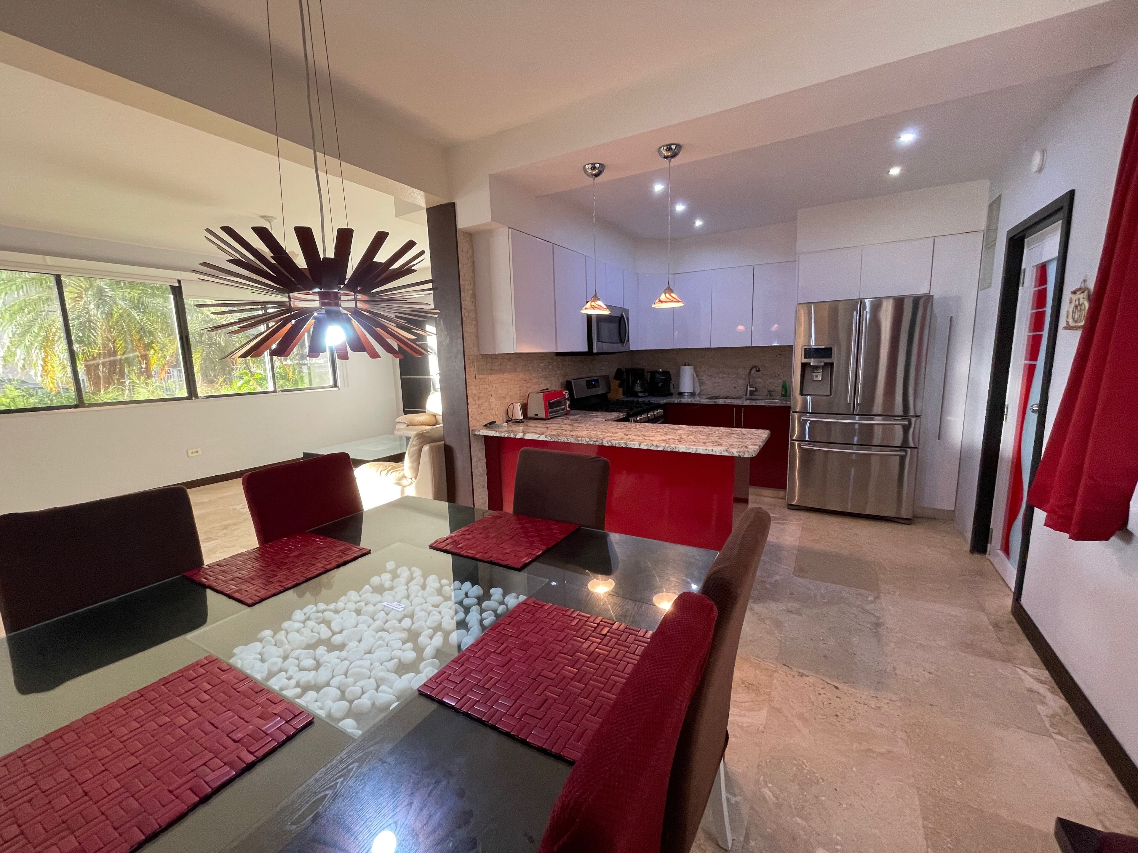 A modern kitchen with a central island, stainless steel appliances, and a dining area with red accents.