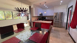 Een moderne keuken met een centraal eiland, roestvrijstalen apparatuur en een eethoek met rode accenten.